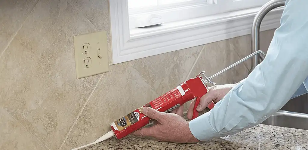 Handyman applying caulk along a kitchen backsplash and countertop seam in Toledo, OH