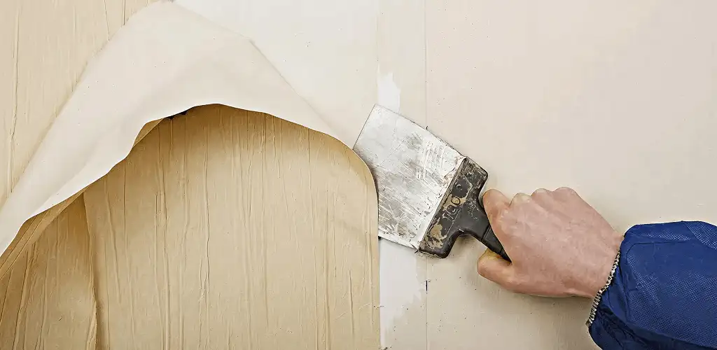 Handyman removing wallpaper with a scraper for wall preparation in Toledo, OH